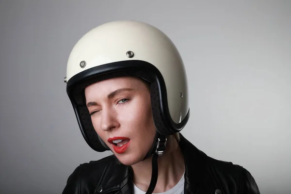 バイカーの若い女性のクローズアップ肖像画、面白い顔をして、赤い唇で白いヘルメットをかぶって。スタジオの背景. — ストック写真