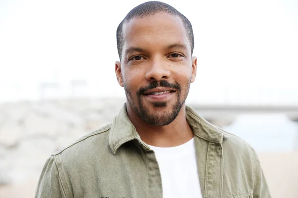 Plajda gülen siyah sakallı yakışıklı bir adamın resmi. Günlük kıyafetler giyiyor. Metnin için boşluk.