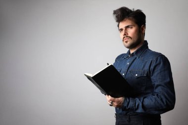 Yapılacaklar listesi yazılıyor. Tişörtlü, kendine güvenen olgun bir adam beyaz arka plan üzerine not defterine bir şeyler yazıyor. Metin için boşluk.