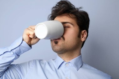 Koyu saçlı sakallı hippi kahve içer. İşadamı bakımlı, kahve molası veren mavi arka planda..