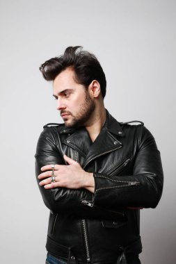 Deri ceketli, beyaz arka planda poz veren modern stil sahibi hippi bir adamın dikey portresi..