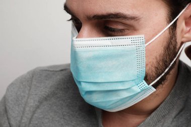 Yüzünde mavi bir tıbbi virüs maskesi olan beyaz bir adamın yan portresi. Koronavirüs ve güvenlik teması. Yatay.