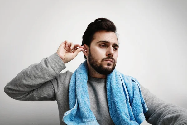 Retrato de un joven barbudo con toalla borrosa limpiando la oreja con cogollos de algodón haciendo su rutina matutina. Espacio para texto . — Foto de Stock