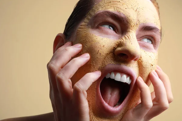 Detailní záběr mladé ženy s hliněnou maskou na tváři křičící na béžovém pozadí, prostor pro text. Péče o kůži. — Stock fotografie