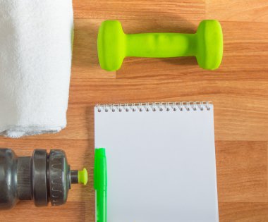 Halter ile egzersiz planı havlu, su şişesi, ahşap arka plan üstünde not etmek