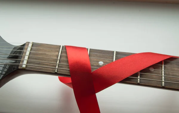 Guitar, rock music and red ribbon - symbol of fight against AIDS — Stock Photo, Image