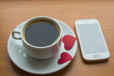 Cep telefonu, ahşap bir masa üzerinde kırmızı kalpler ile kahve fincanı