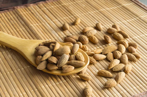 Cucchiaio di legno con mandorle su un tovagliolo di bambù — Foto Stock