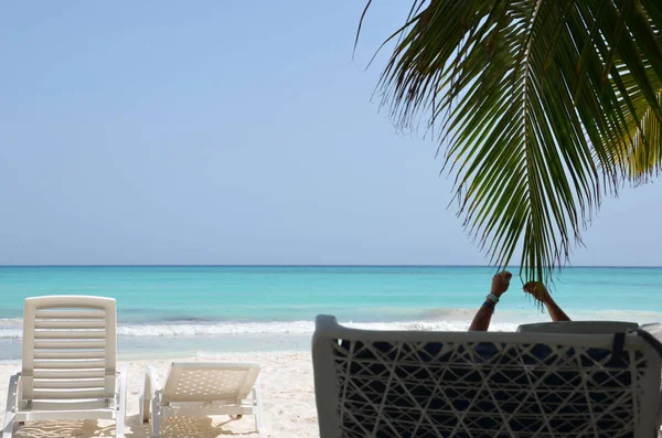 Hermoso mar y arena blanca. Un hombre yace en la tumbona, levantando las manos, a la sombra de palmeras en la playa . — Foto de Stock