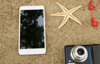 Seyahat planlama ve deniz kum tatile kavramı. Ana sayfa görünümü smartphone, kamera, deniz yıldızı, kulaklık