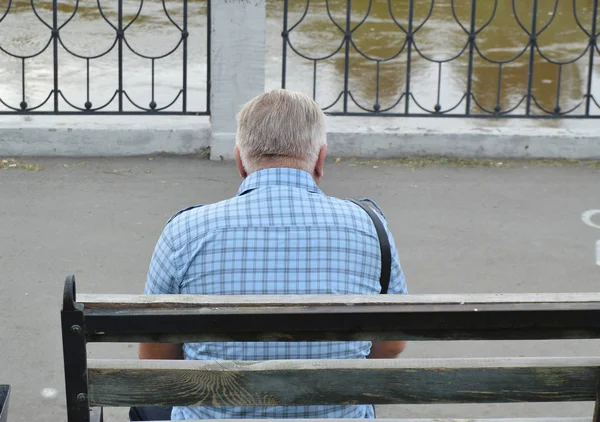 Solitario pensionista anciano sentado en un banco cerca del río, la vista desde la parte posterior —  Fotos de Stock