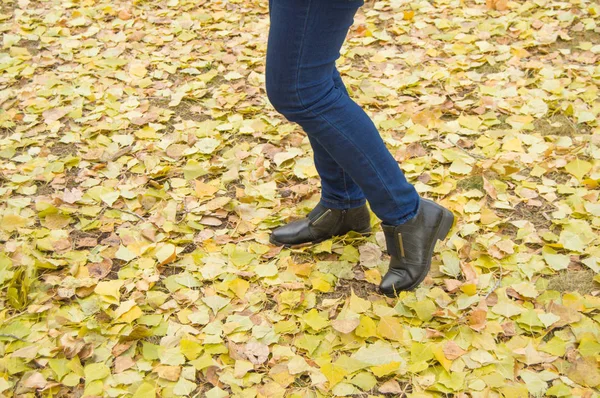 Kobieta nogi z światło niebieskie jeansy i czarne buty w Pomarańczowe jesienne liście — Zdjęcie stockowe