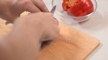 Closeup el kesme kırmızı biber bir kesme tahtası üzerinde mans ve bir cam kaseye