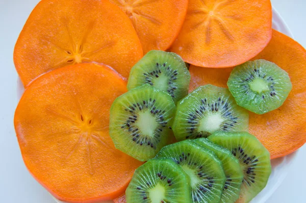 Verse rijpe sappige Kiwi plakjes met persimmon gerangschikt op een plaat, bovenaanzicht — Stockfoto