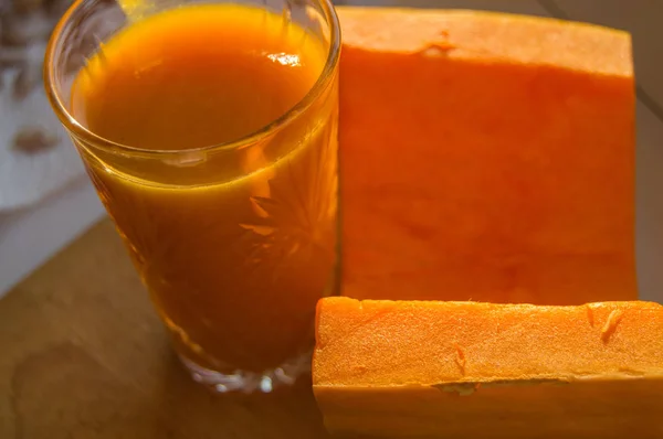 O smoothie de abóbora em um copo e corte a abóbora crua no fundo de madeira — Fotografia de Stock