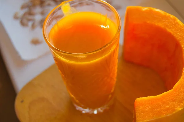 The pumpkin smoothie in a glass and cut raw pumpkin on wooden background