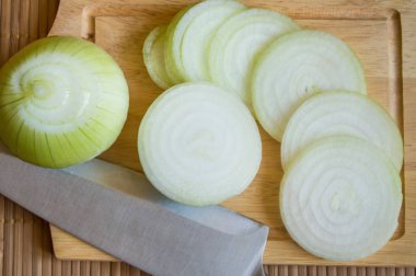 Soğan, dilimlenmiş bir bıçakla ahşap kesme tahtası üzerinde