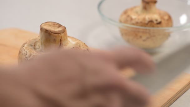 De mannenhand rauwe paddestoelen snijdt met een mes op de cutting Board en vouwt ze in een glazen kom — Stockvideo