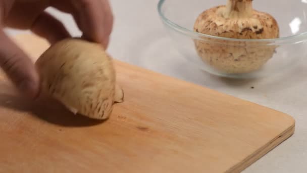 La mano maschile taglia i funghi crudi con un coltello sul tagliere e li piega in una ciotola di vetro — Video Stock