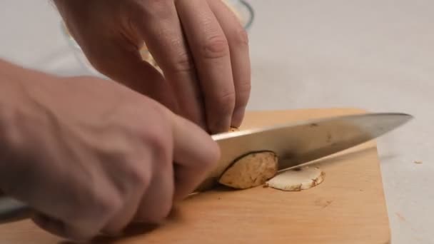 La mano masculina corta hongos crudos con un cuchillo en la tabla de cortar y los pliega en un recipiente de vidrio — Vídeo de stock