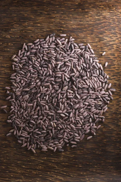 Dark purple rice on dark wooden background, vertical frame illuminated by sunlight — Stock Photo, Image