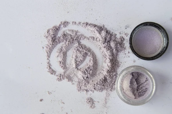 Pearlescent sparkling eye shadow scattered on the table, a jar of shadows