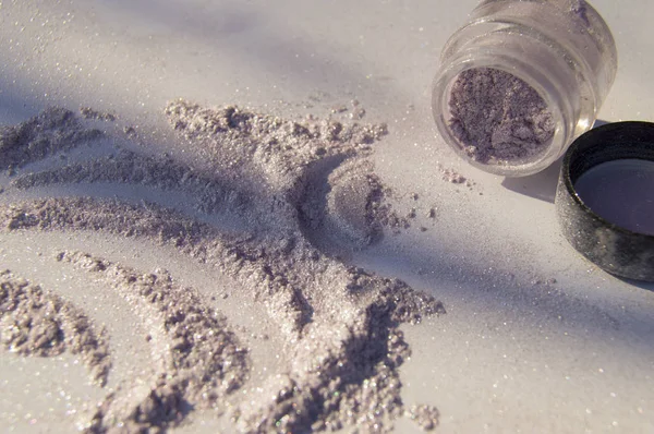 Pearlescent sparkling eye shadow scattered on the table, a jar of shadows