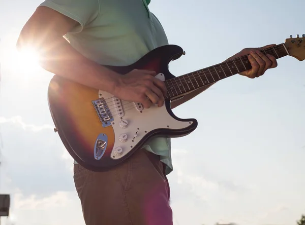 Young man standing with a guitar on background of sky and sunlight — Stock Photo, Image