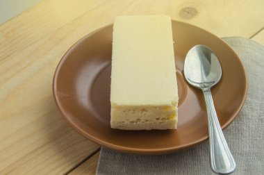 Kahverengi seramik tabakta New York 'un vanilyalı cheesecake' inin iştah açıcı bir parçası, küçük bir kaşık, ahşap kırsal arka plan ve keten peçete.