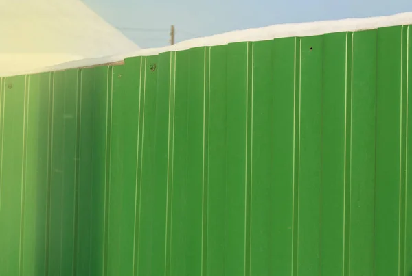 Modern green metal corrugated siding fence, outdoor winter space, safety and security, veneer texture