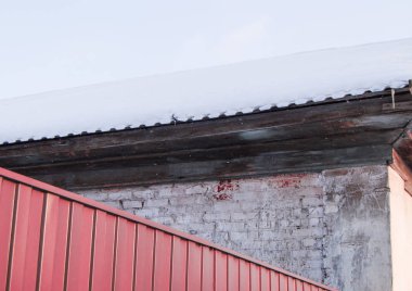 Çitin yan tarafındaki kırmızı metal çarşaf, bir kış günü binayı tuğla duvarla kaplıyor, çatı karla süpürülüyor.