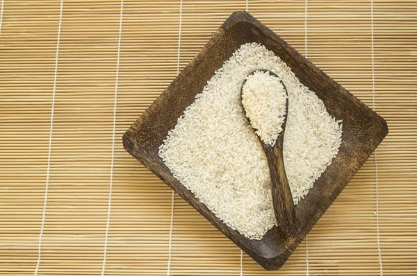 Arroz blanco crudo en plato de madera y cucharas de madera con arroz en servilleta de bambú para una alimentación saludable, vegetarianismo, vista superior, puesta plana — Foto de Stock