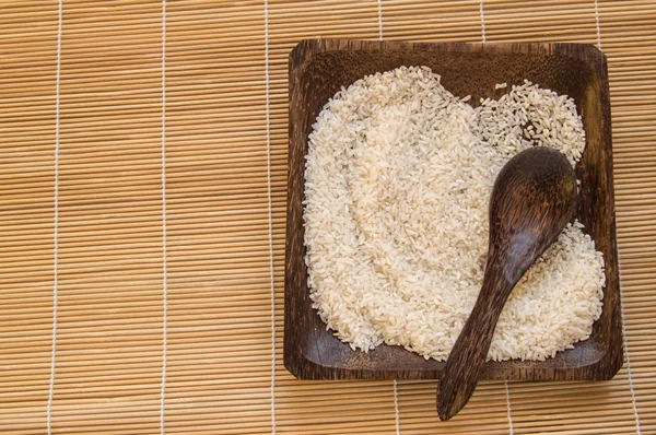 Arroz branco cru em placa de madeira e colheres de madeira com arroz em guardanapo de bambu para alimentação saudável, vegetarianismo, vista superior, flat lay — Fotografia de Stock