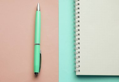 Boş sayfaları olan sarmal defter ve pastel pembe ve nane arkaplanlı dolmakalem, üst görünüm, düz yatış