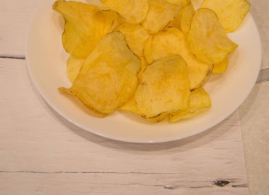 Lezzetli patates cipsleri yuvarlak şekilli, beyaz bir tabakta, arka planda açık ahşap bir masa, üst manzara.