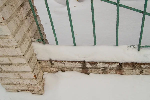 Starý plot s kovovými tyčemi a cihlovými sloupky, popraskaná omítka v důsledku nepříznivých povětrnostních podmínek, venku, sníh, zima, zima — Stock fotografie