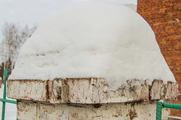 Su un vecchio palo di mattoni con intonaco incrinato si trova un grande cumulo di neve, uno sfondo invernale con una copia dello spazio — Foto Stock