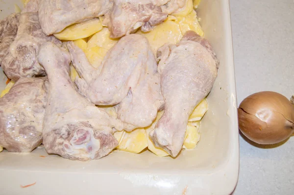 Κομμάτια από ωμό κοτόπουλο μαριναρισμένο σε σάλτσα και πατάτες σε φέτες βρίσκονται σε ένα κεραμικό ταψί, μαγειρεύοντας ένα νόστιμο σπιτικό γεύμα — Φωτογραφία Αρχείου