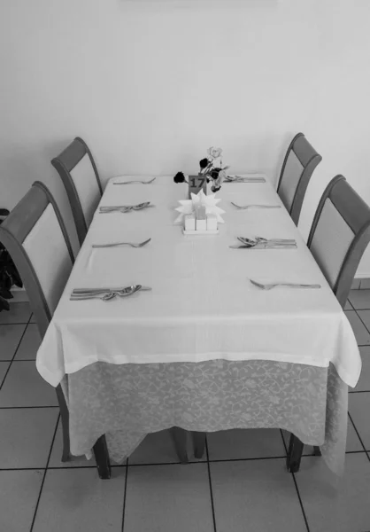 Святковий стіл з скатертиною і столовими приборами в готельному ресторані чекають гостей, вертикальний постріл, вид збоку, чорно-біла рамка — стокове фото