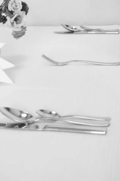 Close-up of elegant silver Cutlery on an empty, white set table, serving waiting for guests, vertical black-and-white frame — Stock Photo, Image