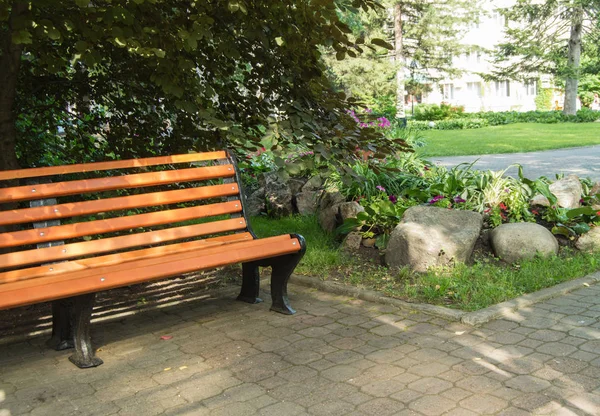 Часть деревянной скамейки возле клумбы с цветами и камнями в солнечный летний день в городском парке — стоковое фото