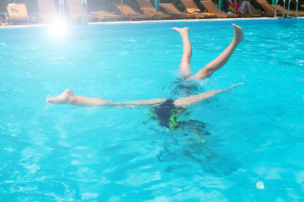 Дети подростки весело плавают и ныряют в открытом бассейне, ноги вверх над водой, брызги, солнечный свет, блики, летний день
