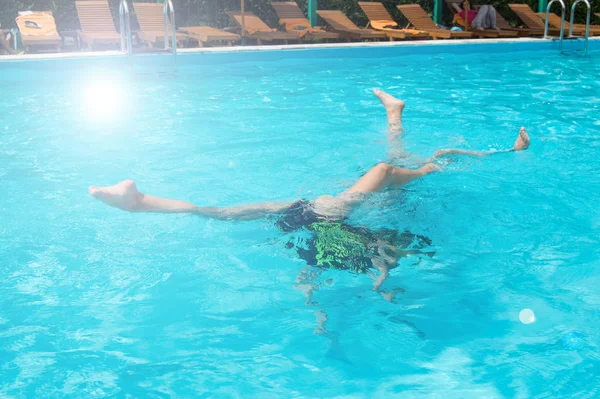 Дети подростки весело плавают и ныряют в открытом бассейне, ноги вверх над водой, брызги, солнечный свет, блики, летний день — стоковое фото