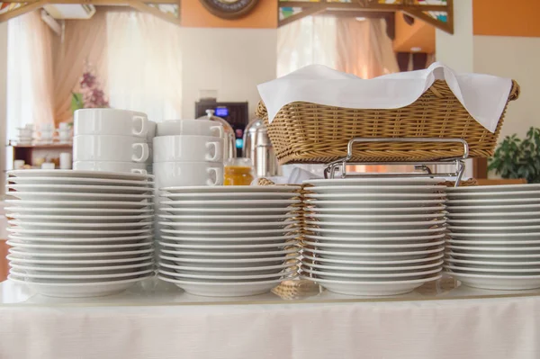 Närbild av en grupp vita keramiska tekoppar och tallrikar står på ett bord med en vit duk, rena rätter i hotellets restaurang tillagad för gästernas frukost — Stockfoto