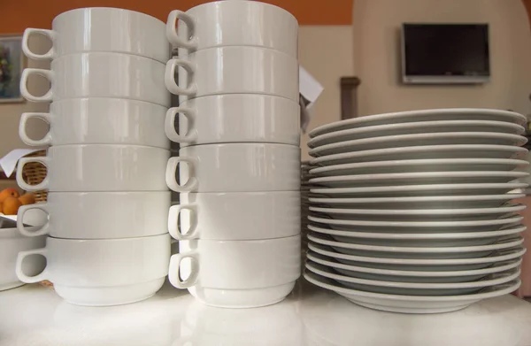 Primer plano de un grupo de tazas de té de cerámica blanca y platos de pie sobre una mesa con un mantel blanco, platos limpios en el restaurante del hotel preparado para el desayuno de los huéspedes — Foto de Stock