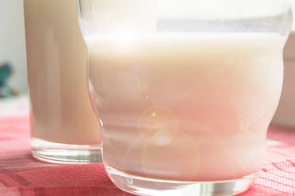 Detailní záběr dvou sklenic mléka na kostkovaném červeném ubrousku, slunečním svitu, zdravém pojetí jídla a diety pro děti i dospělé — Stock fotografie