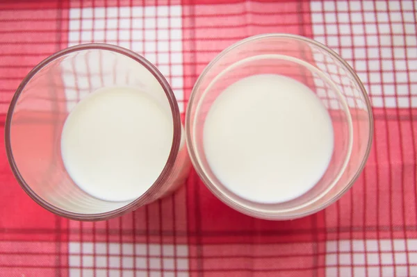 Vista superior dois copos de leite em um guardanapo vermelho xadrez, luz solar, comida saudável e conceito de bebida dietética para crianças e adultos — Fotografia de Stock