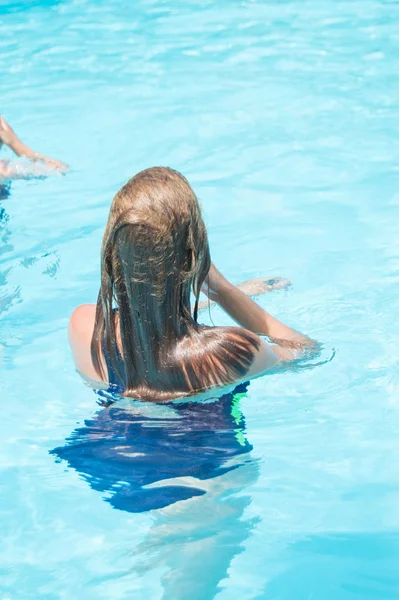 Счастливая девушка с мокрыми волосами, стоящая в воде в открытом бассейне, развлекающаяся в воде на отдыхе, вертикальное фото, вид сзади — стоковое фото