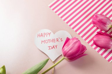 Delicate pink background with flowers of tulips, a card, a heart that says mother's day. Women's day. Postcard for Valentine's Day, on March 8
