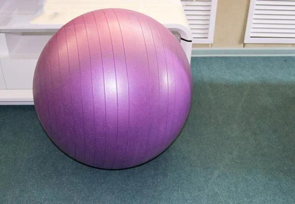 Equipamento desportivo para um estilo de vida saudável-bola de fitness roxo em um ginásio vazio no chão — Fotografia de Stock